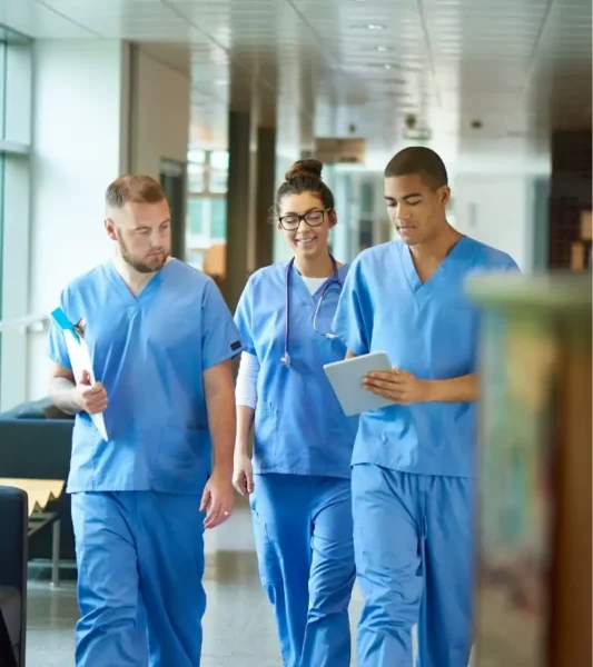 Una persona con guantes médicos azules utiliza un paño de limpieza amarillo para limpiar una superficie metálica reflectante en lo que parece ser un entorno sanitario o de laboratorio, con equipos científicos difuminados al fondo.